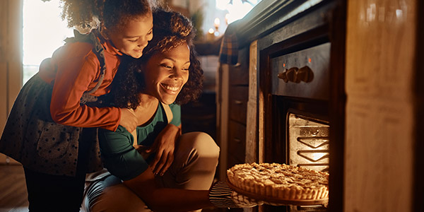 mother and daughter taking a pie out of the oven