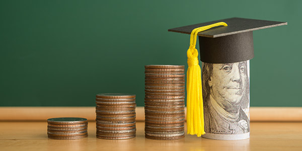 stacks of coins and a roll of cash with a graduation cap on top