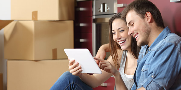 young, happy couple sitting on the kitchen floor on their tablet while  moving into their new home