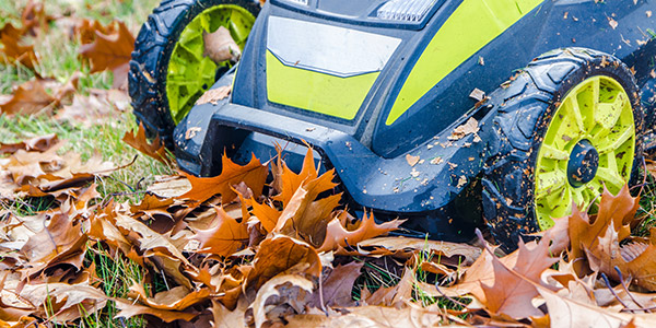 A lawn mower rolls over dried fall leaves on the ground
