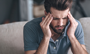 Mlad moški se drži za glavo zaradi bolečin in se sprašuje, če ni zanjo morda kriv tumor v glavi.