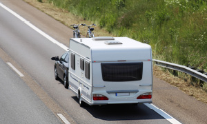 Vleka počitniške prikolice s črnim družinskim avtom na poletno kampiranje.