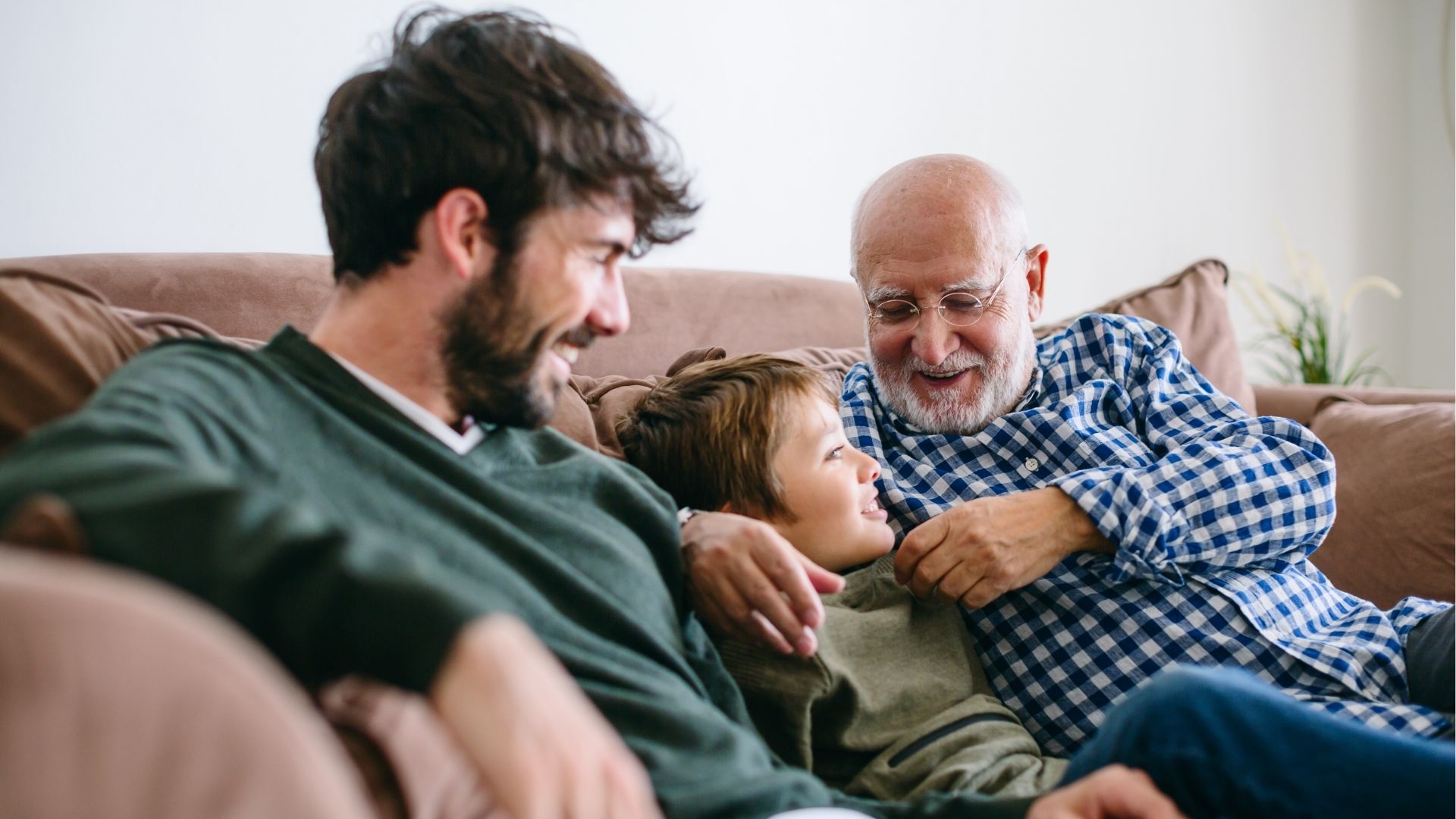 Granddad and Dad relaxing on a sofa with a child, spending quality time together.