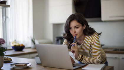 Woman sitting at a wooden table looking at a laptop 