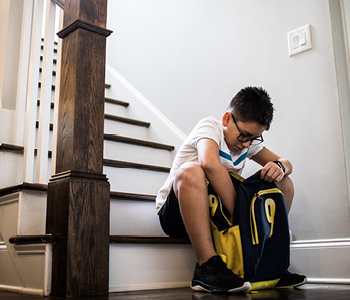 Deček zjutraj pred odhodom v šolo v veži hiše preverja vsebino svoje šolske torbe