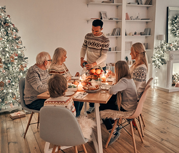 Družina sedi za praznično okrašeno mizo in skupaj uživa večerjo.