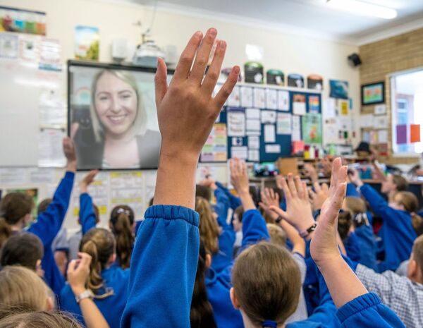 A school class raising their hands while a Kids Helpline counsellor smiles on screen