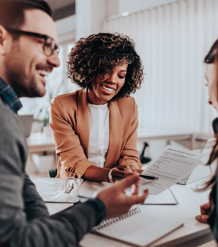 Professional African American woman helping happy couple across her desk with paperwork 
