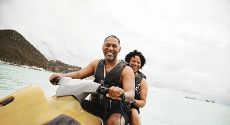 African American man and woman riding on a yellow jet ski smiling. 