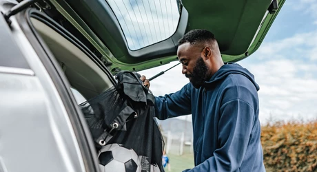 Soccer coach arriving to a practice taking a duffel bag with balls out the trunk of his car. 
