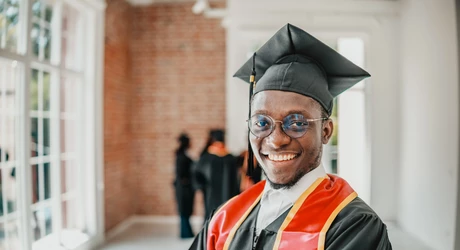 Male graduate in cap and gown with red and yellow honor stole. 