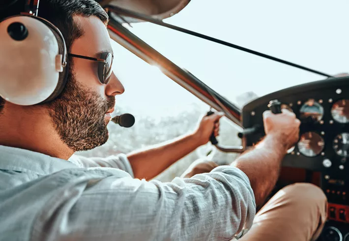 Young man with beard in an airplane cabin flying a plane. Side, close view of pilot. 