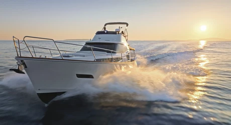 Couple driving a white yacht through the ocean. Sun is setting in the background. 